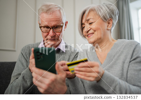 Senior couple man woman shopping online with smartphone paying with credit card. Old people buying on Internet enter credit card details at home indoors. Online shopping delivery service ecommerce 132834537