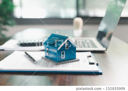 House model placed on table alongside coins, paperwork symbolizes real estate investment, property valuation, representing financial planning, mortgage options, market analysis in property business. 132835009