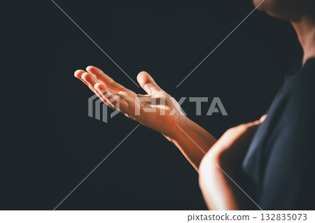 Dark silence of the church, a Christian lifts their hand in prayer to God, a symbol of worship, faith, and hope-embracing the spiritual concept of religion and believing in Jesus Christ. Dark silence of the church, a Christian lifts their hand in prayer to God, a symbol of worship, faith, and hope-embracing the spiritual concept of religion and believing in Jesus Christ. 132835073