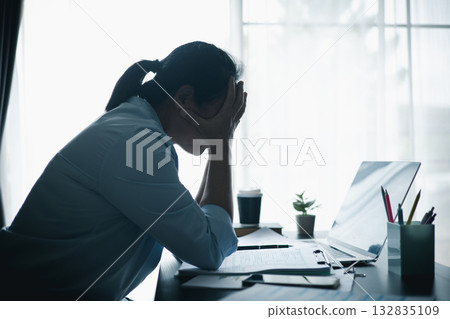 Asian woman sitting at desk with laptop, hands clasped under chin, looking stressed and thoughtful, symbolizing workplace burnout, mental health struggles or silent prayer for hope. Asian woman sitting at desk with laptop, hands clasped under chin, looking stressed and thoughtful, symbolizing workplace burnout, mental health struggles or silent prayer for hope. 132835109