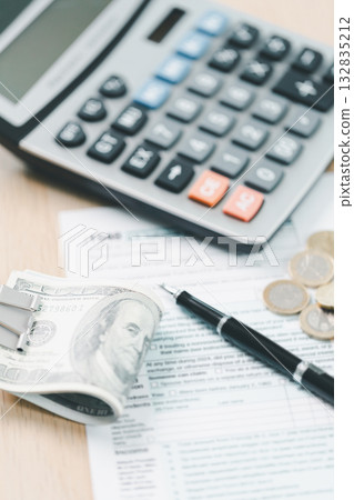Concept of tax season and financial accounting. Stack of US dollar bills clipped on income tax forms, symbolizing payment, business finance, budget management and personal income report. Concept of tax season and financial accounting. Stack of US dollar bills clipped on income tax forms, symbolizing payment, business finance, budget management and personal income report. 132835212