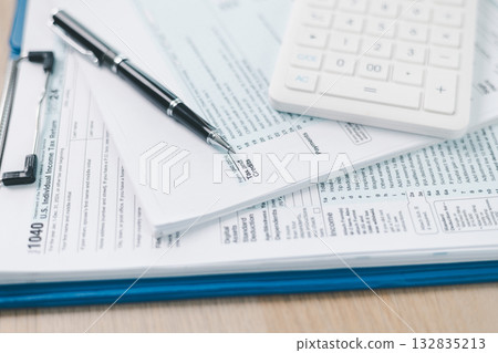 Concept of tax filing and accounting. Close up of US individual income tax return form with pen and calculator on office desk, symbolizing financial planning, budget management and payment accuracy. 132835213