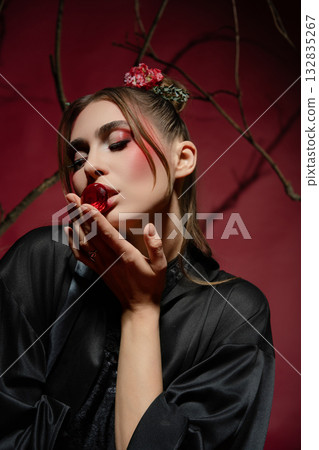 Model poses with a red flower, exuding elegance against a dark backdrop Model poses with a red flower, exuding elegance against a dark backdrop 132835267