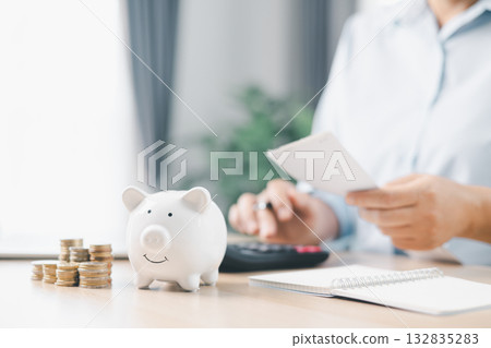 Concept of saving money and investment planning. A businesswoman drops coin into white piggy bank on office desk with documents, symbolizing financial security, budget management and future wealth. 132835283