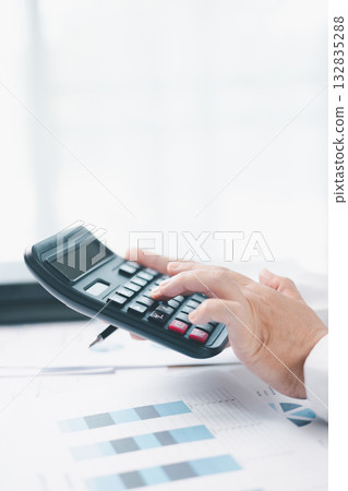 Close up of businesswoman using calculator for financial analysis and accounting on office desk with charts and reports. Concept of business planning, budget calculation and investment strategy. 132835288