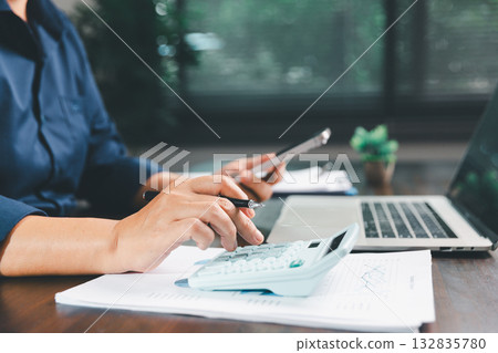 Office businesswoman hand to operate calculator analyzing financial data, counting costs on desk. accounting, financial analysis for business budget planning, calculation support, finance management. 132835780