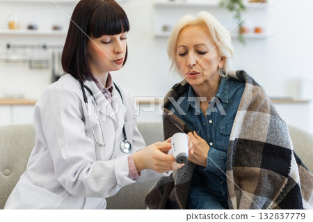A doctor is checking the temperature of an elderly woman using a digital thermometer. The woman is wrapped in a blanket. A doctor is checking the temperature of an elderly woman using a digital thermometer. The woman is wrapped in a blanket. 132837779