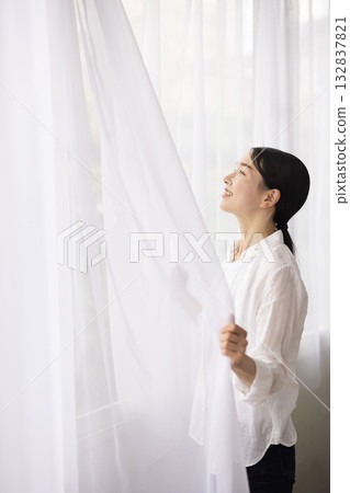 A woman opens the curtains and bathes in the morning light A woman opens the curtains and bathes in the morning light 132837821