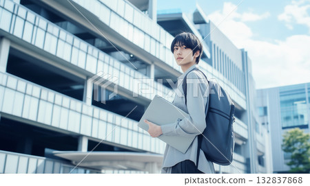 Young handsome Asian male student standing in front of a building with a laptop 132837868