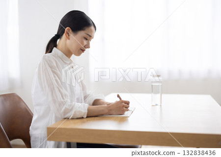 一位中年婦女坐在桌旁，用筆記本做筆記。 132838436