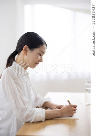 一位中年婦女坐在桌旁，用筆記本做筆記。 132838437