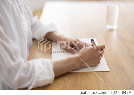 Hands of a woman in a white shirt writing in a notebook 132838439