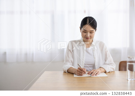 A middle-aged woman taking notes in a notebook at a table 132838443