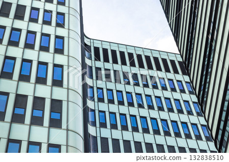 Abstract architecture with geometric patterns and blue window panes. Modern office building design reaching towards the sky. Urban skyline. Abstract architecture with geometric patterns and blue window panes. Modern office building design reaching towards the sky. Urban skyline. 132838510