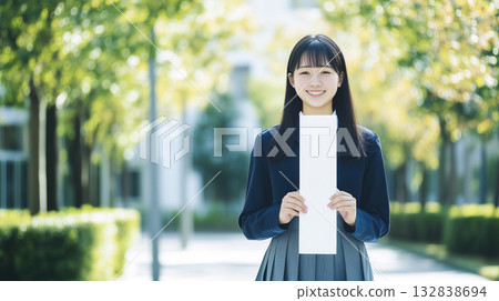 A high school girl in uniform holding a vertical blank piece of paper in front of her chest 132838694
