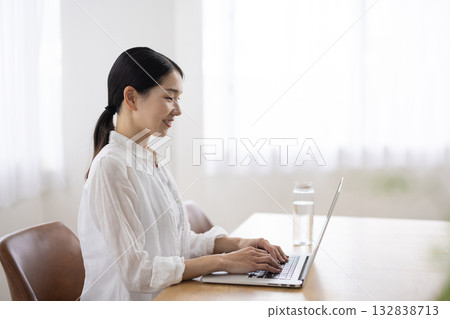 一位中年婦女在餐桌上操作筆記型電腦。 132838713