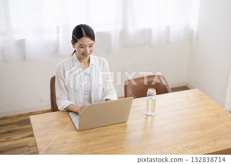 一位中年婦女在餐桌上操作筆記型電腦。 132838714