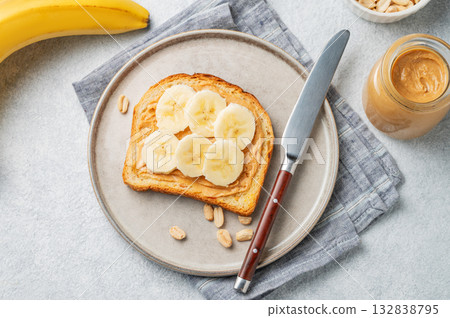 Peanut butter toast and banana in a plate on a light background with nuts and knife. 132838795