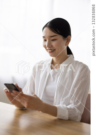 A smiling middle-aged woman operating a smartphone at a table 132838868
