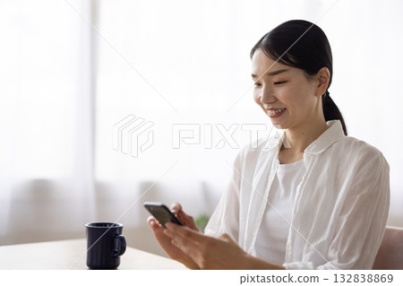 一位微笑的中年婦女正在桌邊操作智慧型手機。 132838869
