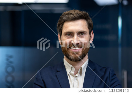 Close-up portrait of a young smiling and successful businessman in the office looking at the camera. Close-up portrait of a young smiling and successful businessman in the office looking at the camera. 132839143