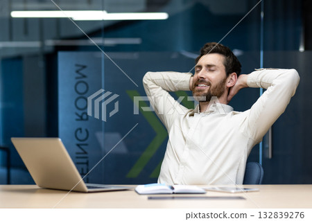 Relaxed smiling young man sitting at a desk in the office, hands behind his head, eyes closed and resting. Relaxed smiling young man sitting at a desk in the office, hands behind his head, eyes closed and resting. 132839276