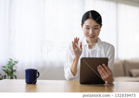 Smiling woman waving at tablet at living room table 132839473