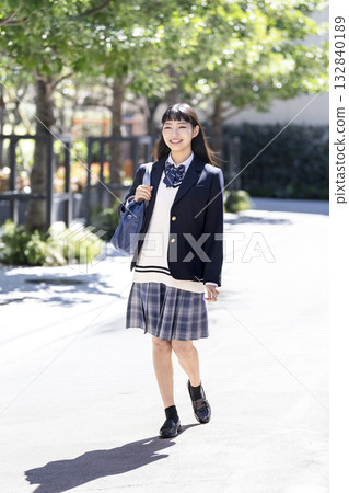 一位面帶微笑的女高中生肩上背著書包走著。 一位面帶微笑的女高中生肩上背著書包走著。 132840189