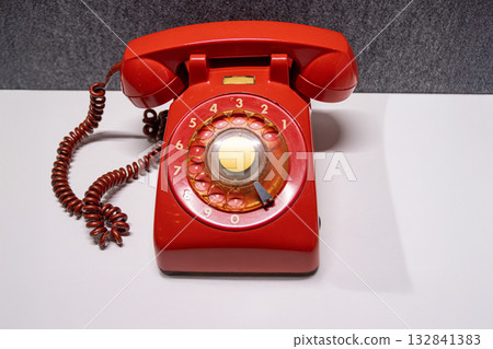 Vintage rotary telephone red retro style. A bright red antique telephone with a gold-tone center dial rests on a white surface, evoking 20th-century communication nostalgia 132841383