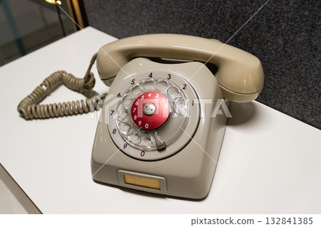 Vintage rotary telephone dial retro classic. A beige grey antique telephone with a red center dial sits on a white surface, representing old technology and communication 132841385