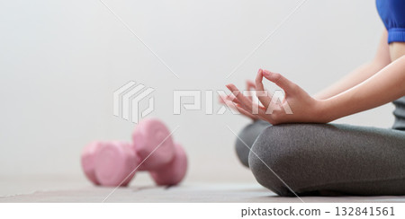 Mindfulness and Fitness: Woman Meditating with Dumbbells in Background Mindfulness and Fitness: Woman Meditating with Dumbbells in Background 132841561