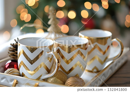 Three stylish gold chevron mugs rest on a decorative tray adorned with ornaments, exuding a warm, festive ambiance perfect for the holidays Three stylish gold chevron mugs rest on a decorative tray adorned with ornaments, exuding a warm, festive ambiance perfect for the holidays 132841800