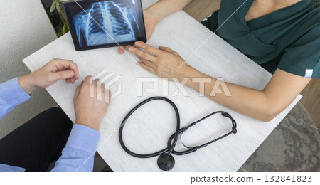 Shot of the female doctor in uniform showing x-ray image of the lungs on the tablet to the patient 132841823
