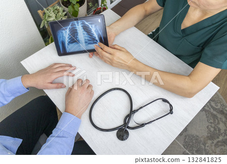 Shot of the female doctor in uniform showing x-ray image of the lungs on the tablet to the patient Shot of the female doctor in uniform showing x-ray image of the lungs on the tablet to the patient 132841825