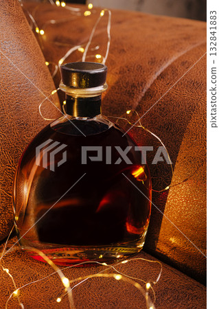 Elegant bottle of liquor surrounded by warm string lights on a cozy couch 132841883