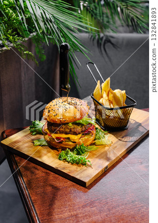 Delicious burger served with crispy fries on a wooden board in a cozy setting Delicious burger served with crispy fries on a wooden board in a cozy setting 132841893
