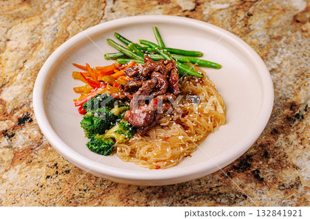 Delicious stir-fried beef with noodles and fresh vegetables on a white plate 132841921