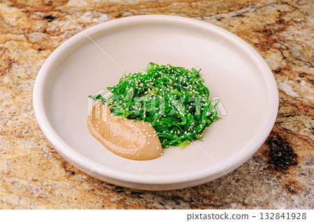 Fresh green seaweed salad with sesame dressing on a stone surface Fresh green seaweed salad with sesame dressing on a stone surface 132841928