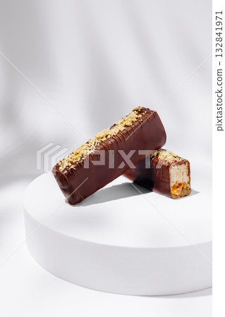 Delicious chocolate bars on a minimal white pedestal showcasing sweet treats Delicious chocolate bars on a minimal white pedestal showcasing sweet treats 132841971