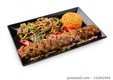 Lamb kebab served with fresh salad and bulgur pilaf on a stylish black plate Lamb kebab served with fresh salad and bulgur pilaf on a stylish black plate 132842049