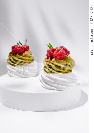 Delicious matcha desserts topped with fresh raspberries on a white pedestal 132842123