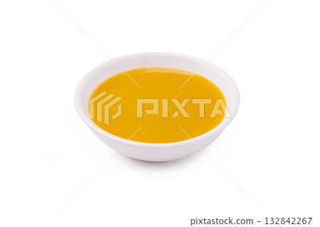 Golden sauce in a small white bowl on a clean surface showcases vibrant color Golden sauce in a small white bowl on a clean surface showcases vibrant color 132842267