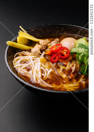 Flavorful bowl of steaming noodle soup with fresh garnishes and spices Flavorful bowl of steaming noodle soup with fresh garnishes and spices 132842335