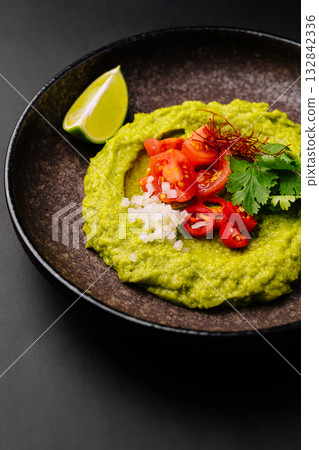 Fresh avocado dip served with colorful toppings on a black plate Fresh avocado dip served with colorful toppings on a black plate 132842336