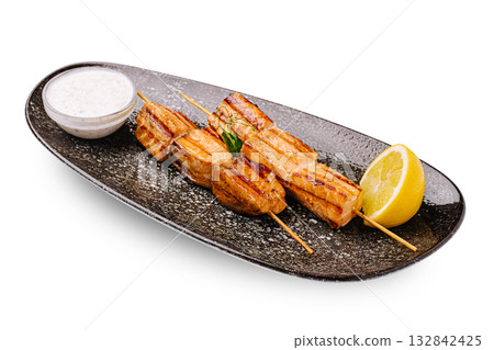 Grilled salmon skewers served with lemon and dipping sauce on a platter 132842425