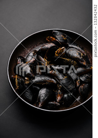 Fresh mussels served in a black bowl on a dark surface for a seafood feast Fresh mussels served in a black bowl on a dark surface for a seafood feast 132842432