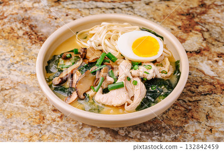 Ramen bowl with chicken, egg, and veggies on a granite counter 132842459