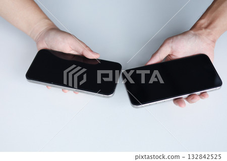 Two people holding smartphones close to each other for initiating a wireless data transfer for exchange data, share photos, documents, and other files by bringing their devices near one another. Two people holding smartphones close to each other for initiating a wireless data transfer for exchange data, share photos, documents, and other files by bringing their devices near one another. 132842525