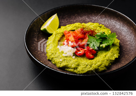 Fresh avocado dip served with toppings on a dark plate 132842576