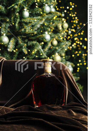 Elegant bottle of whiskey resting on velvet near a festive Christmas tree Elegant bottle of whiskey resting on velvet near a festive Christmas tree 132842582